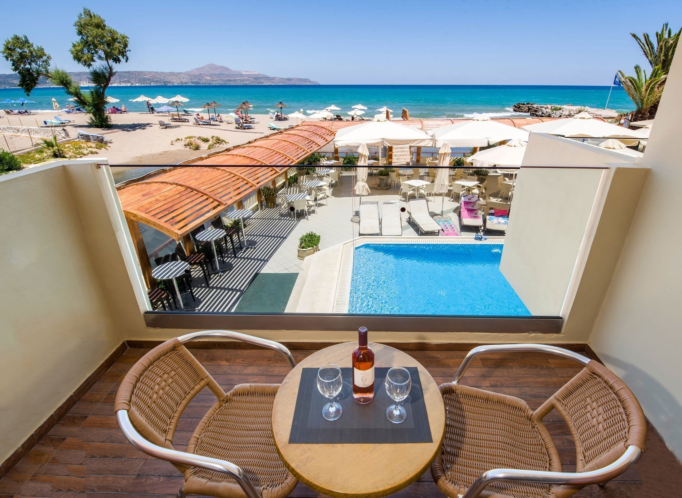 a pool with chairs and a table by it with a beach in the background